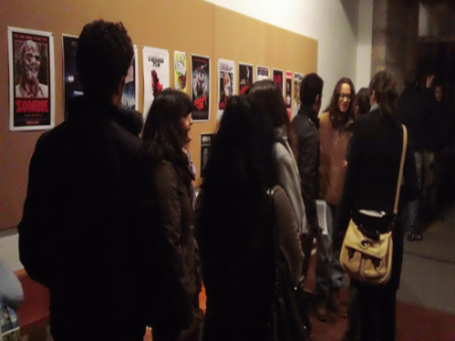 Participantes conversam na entrada do auditório. Em pano de fundo, os cartazes dos filmes em exibição na jornada.